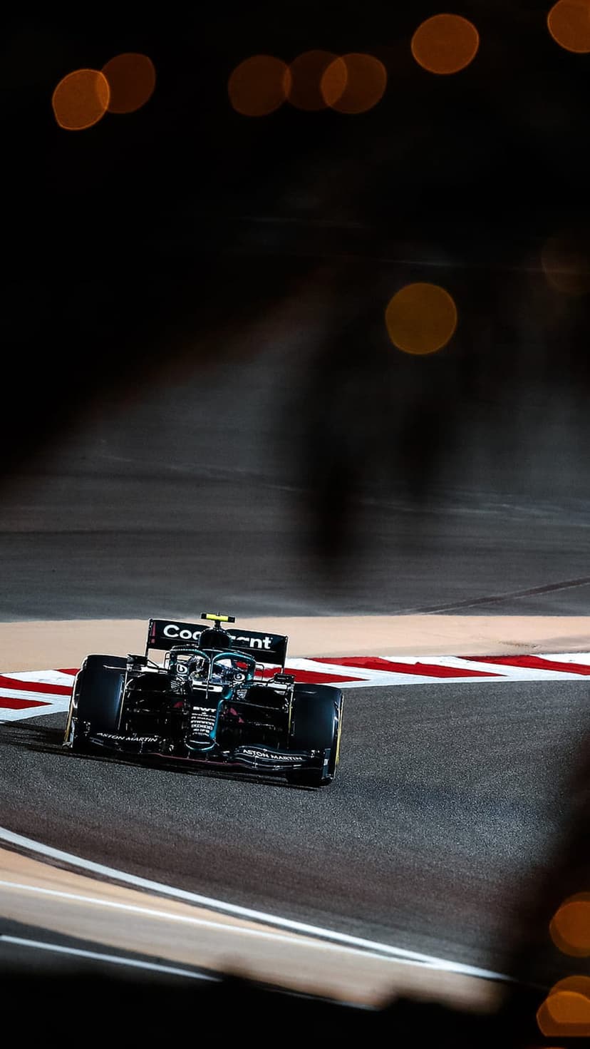 Formula 1 car speeds through a night track corner with blurred golden bokeh lights in the dark background.