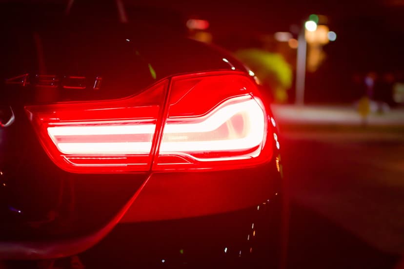 Red LED car taillights glow intensely on a black vehicle with a blurred urban night background in a vertical view.