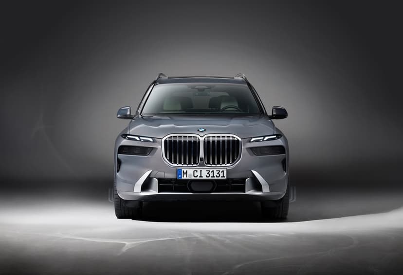 Front view of a grey BMW X7 with glowing split headlights and large chrome grille in a dark studio.