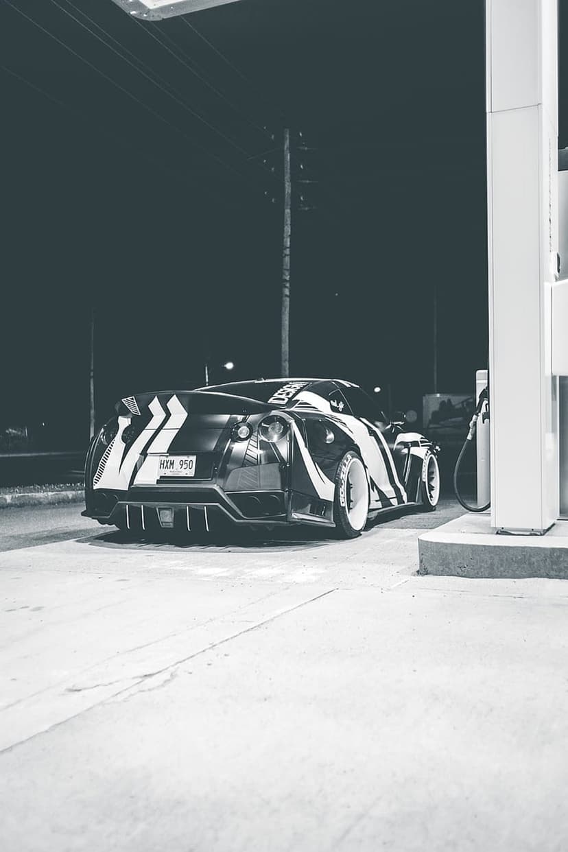 Nissan GT-R with a white graphic wrap parked beside a gas pump at night in a high-contrast black and white style.