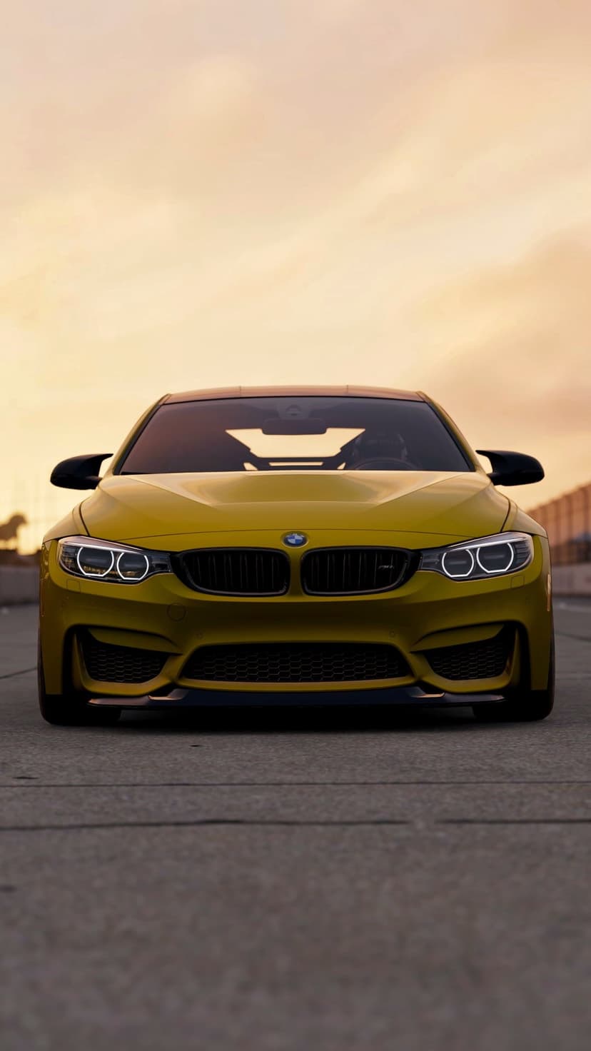 Yellow BMW M4 sports car front view with glowing headlights on a track under a warm orange sunset sky.