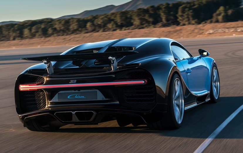 Bugatti Chiron rear view on a track with a blue and black body, active wing, and red LED light bar at sunset.