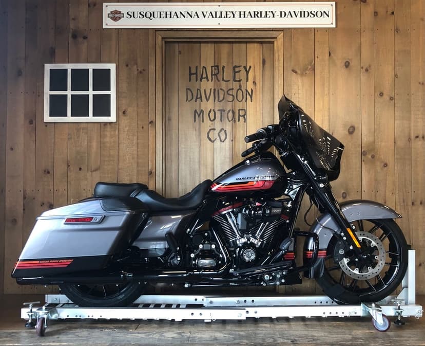 Harley-Davidson CVO motorcycle with gray paint and orange stripes standing against a rustic wooden paneled wall.