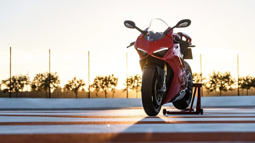 Red Ducati Panigale V4 motorcycle on a racetrack during golden hour with blurred trees and sunset in the background.