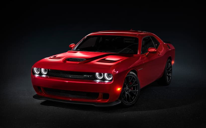 Red Dodge Challenger SRT Hellcat with glowing circular headlights in a dark studio with dramatic lighting.