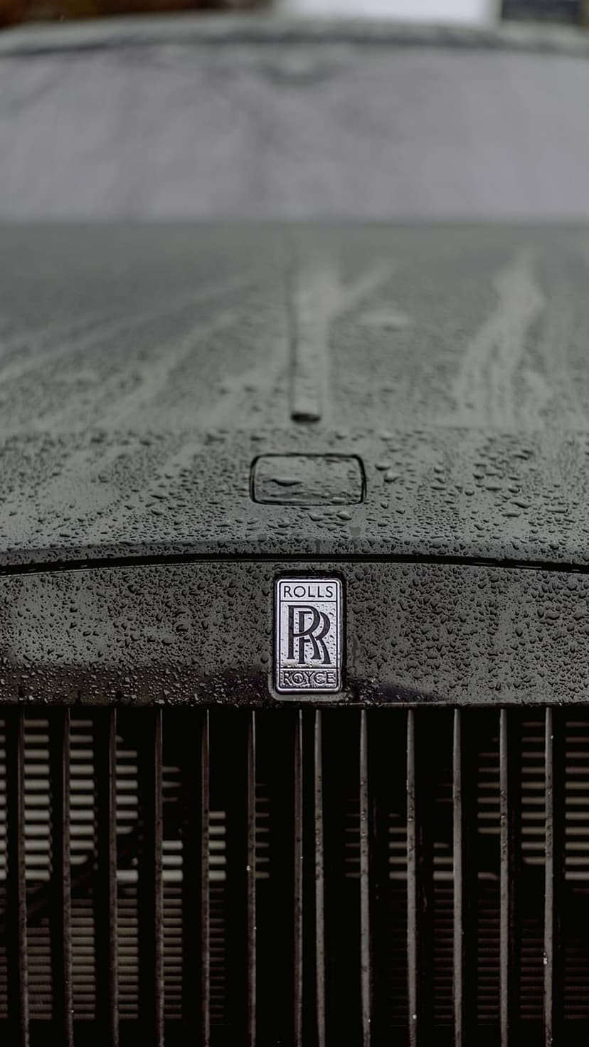 Rolls Royce hood and chrome grille covered in raindrops with the silver emblem visible in a close-up macro shot.