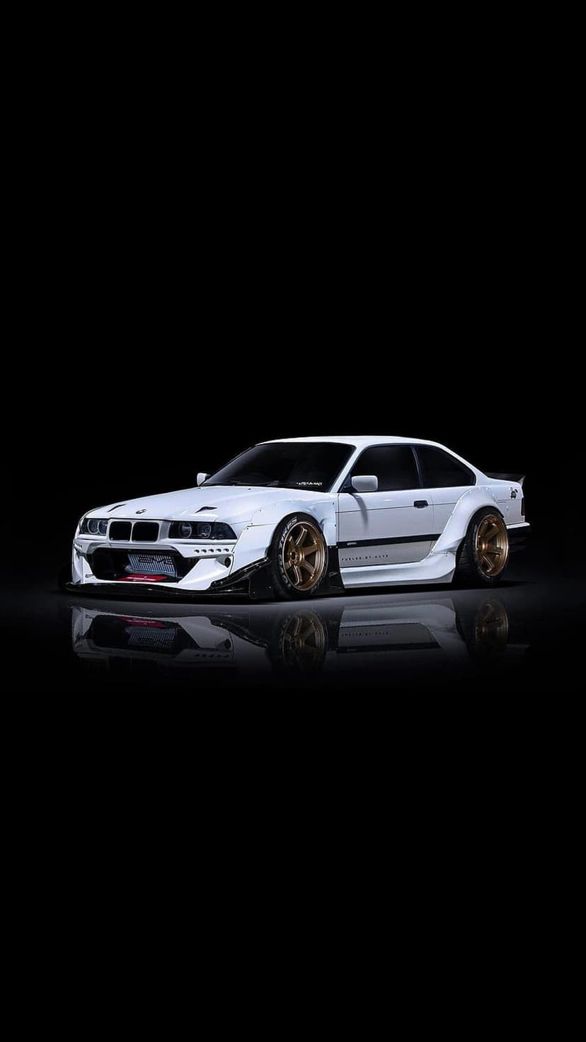 White BMW E36 coupe with widebody flares and bronze multi-spoke wheels against a solid black studio background.