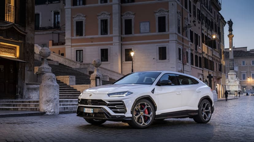 White Lamborghini Urus parked on cobblestones by the Spanish Steps in Rome at dusk with warm city lights.