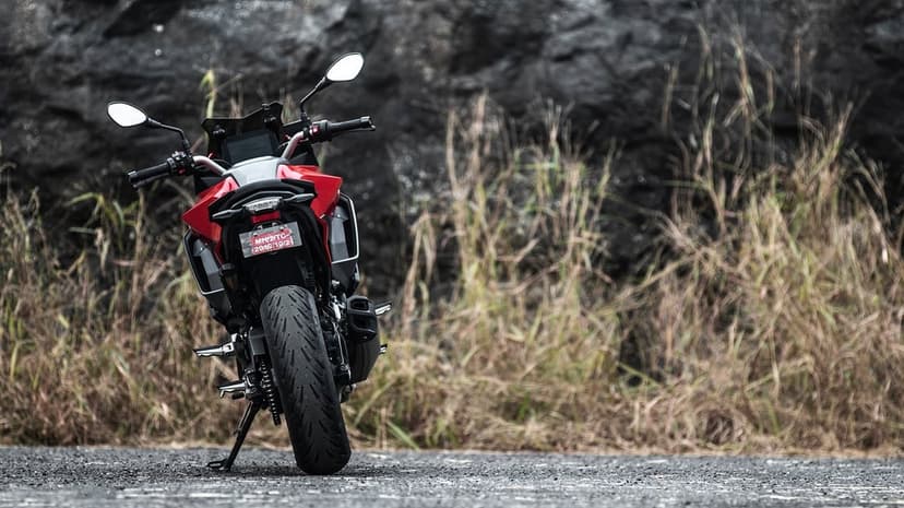 Rear view of a red motorcycle parked on asphalt with a background of dry grass and dark rocky cliffs.
