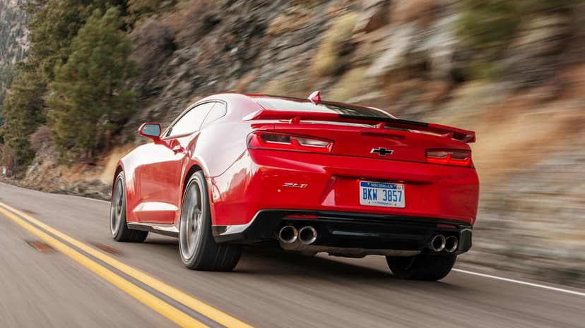 Red Chevrolet Camaro ZL1 driving fast on a mountain road with motion blur and rocky cliffs in the background.