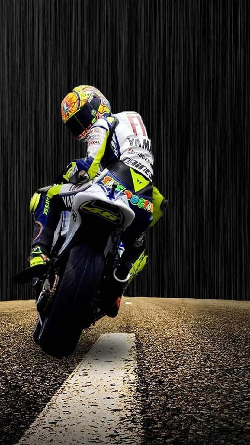 Valentino Rossi leans a Yamaha motorcycle on a wet racetrack with rain mist and a yellow helmet clearly visible.