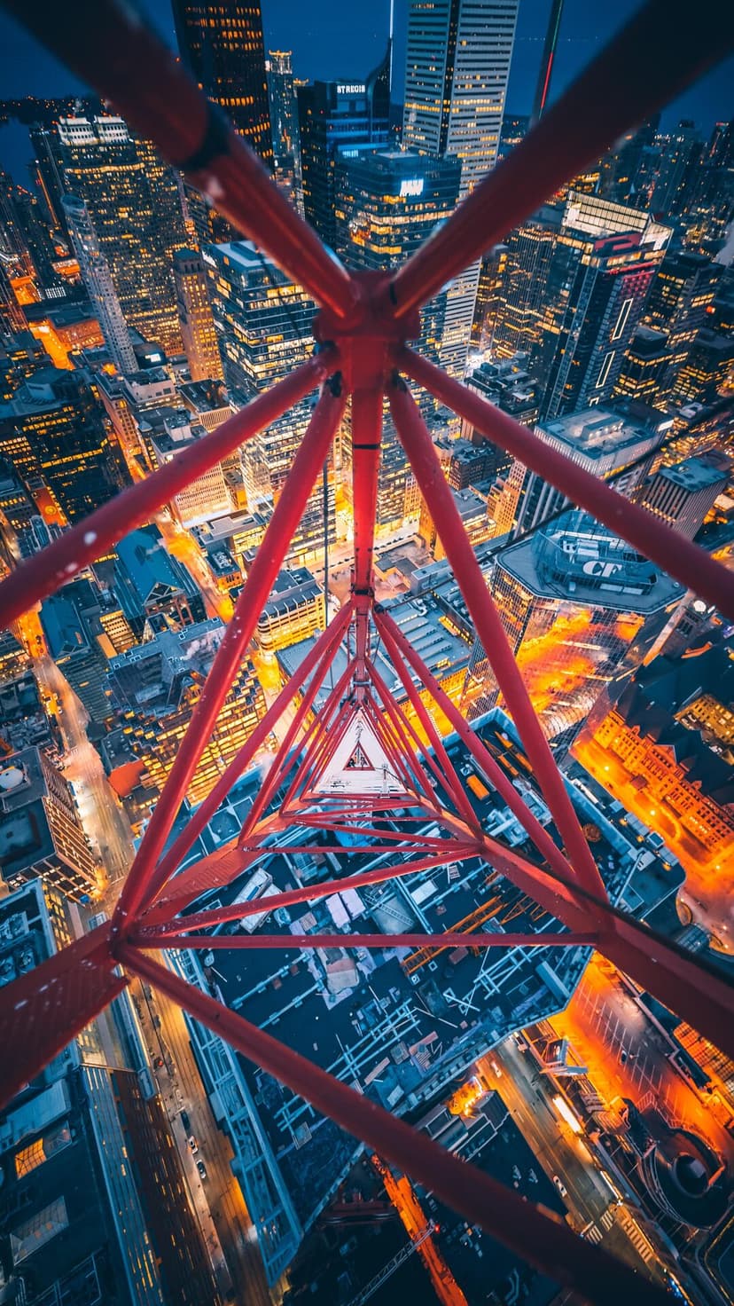 Red steel crane structure forms a geometric pattern above a lit city skyline during blue hour at night.