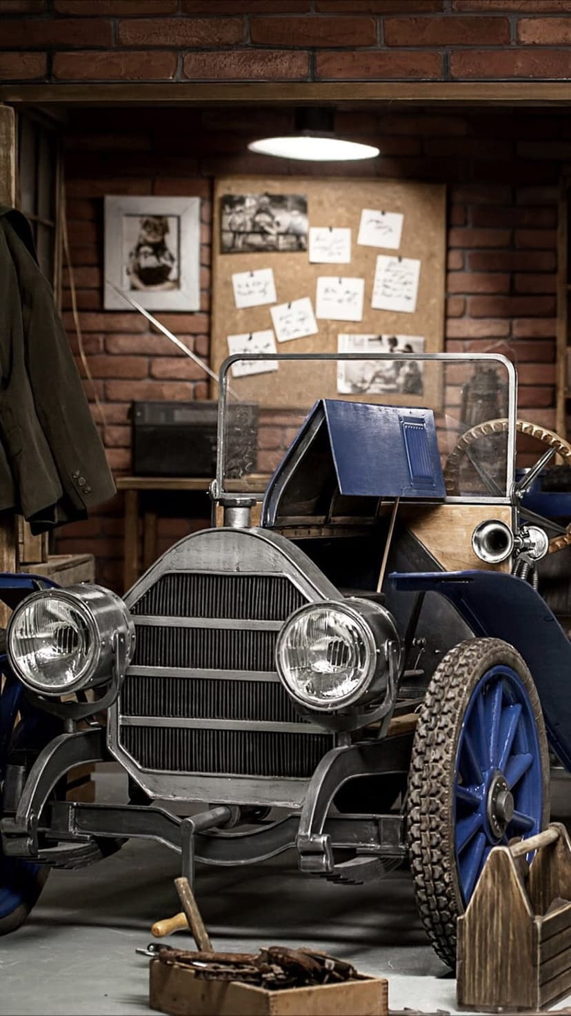 Classic car with blue wheels inside a rustic garage filled with tools, a corkboard, and brick walls.