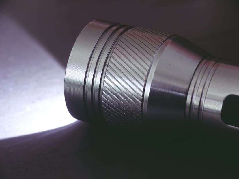 Metal flashlight with a textured grip emits a sharp white light beam against a dark background in close-up.