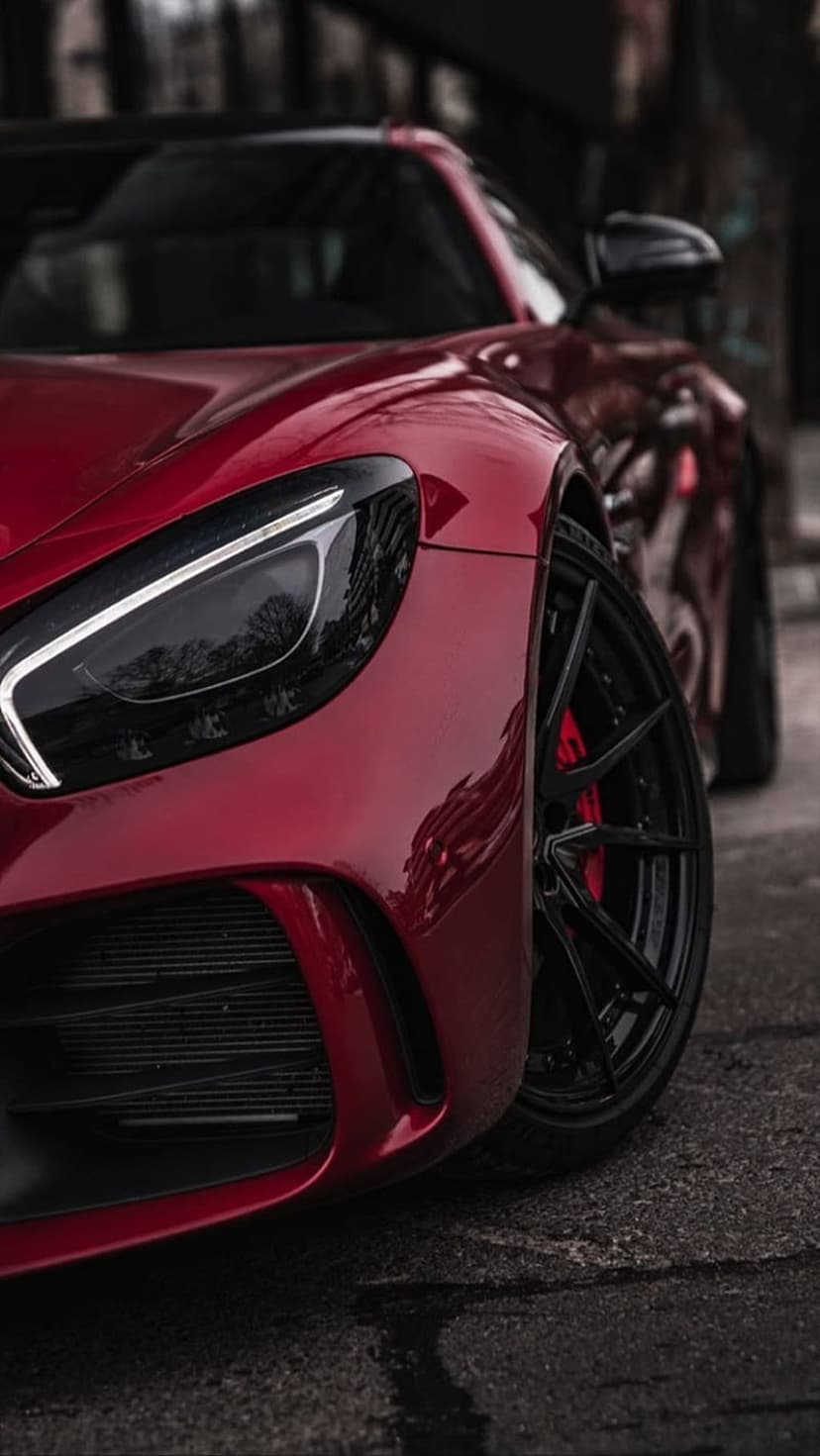 Crimson sports car with sharp LED headlights and black multi-spoke rims resting on a rain-slicked dark pavement.