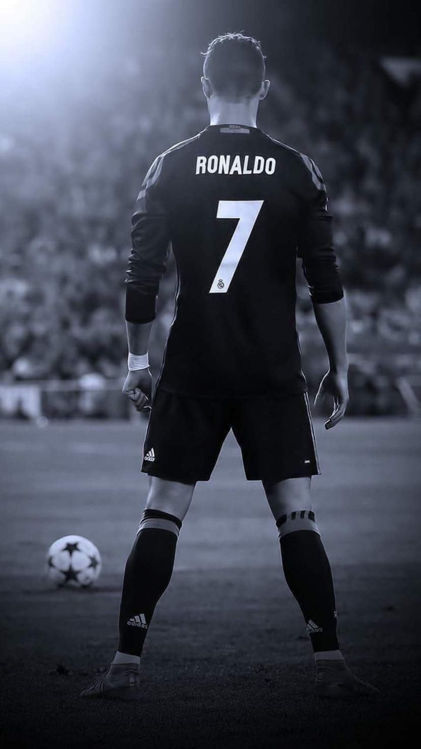 Cristiano Ronaldo in a black number 7 Real Madrid jersey stands over a soccer ball on a dark football pitch.