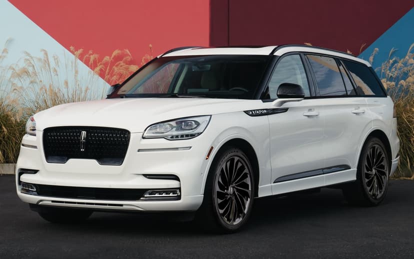 White Lincoln Aviator SUV with black grille and wheels parked against a red and blue geometric background.