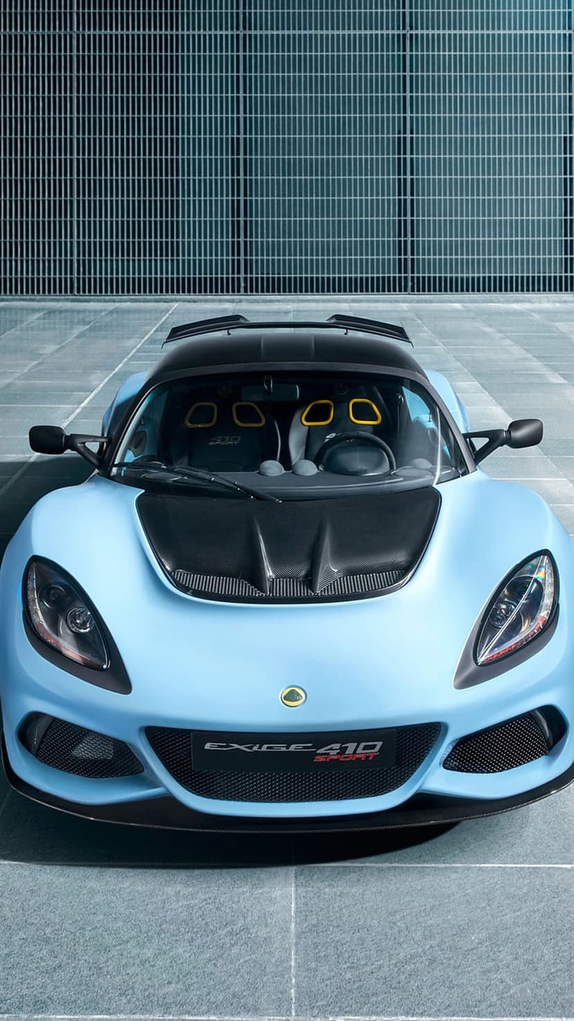 Sky blue Lotus Exige 410 Sport with carbon fiber accents parked against a minimalist grey industrial wall.