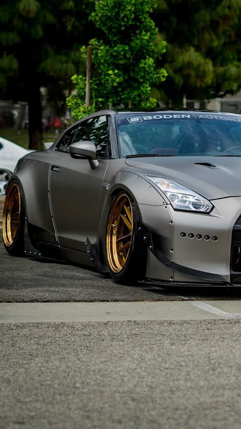 Nissan GT-R widebody with gold multi-spoke rims and exposed bolt fenders parked on an asphalt road.