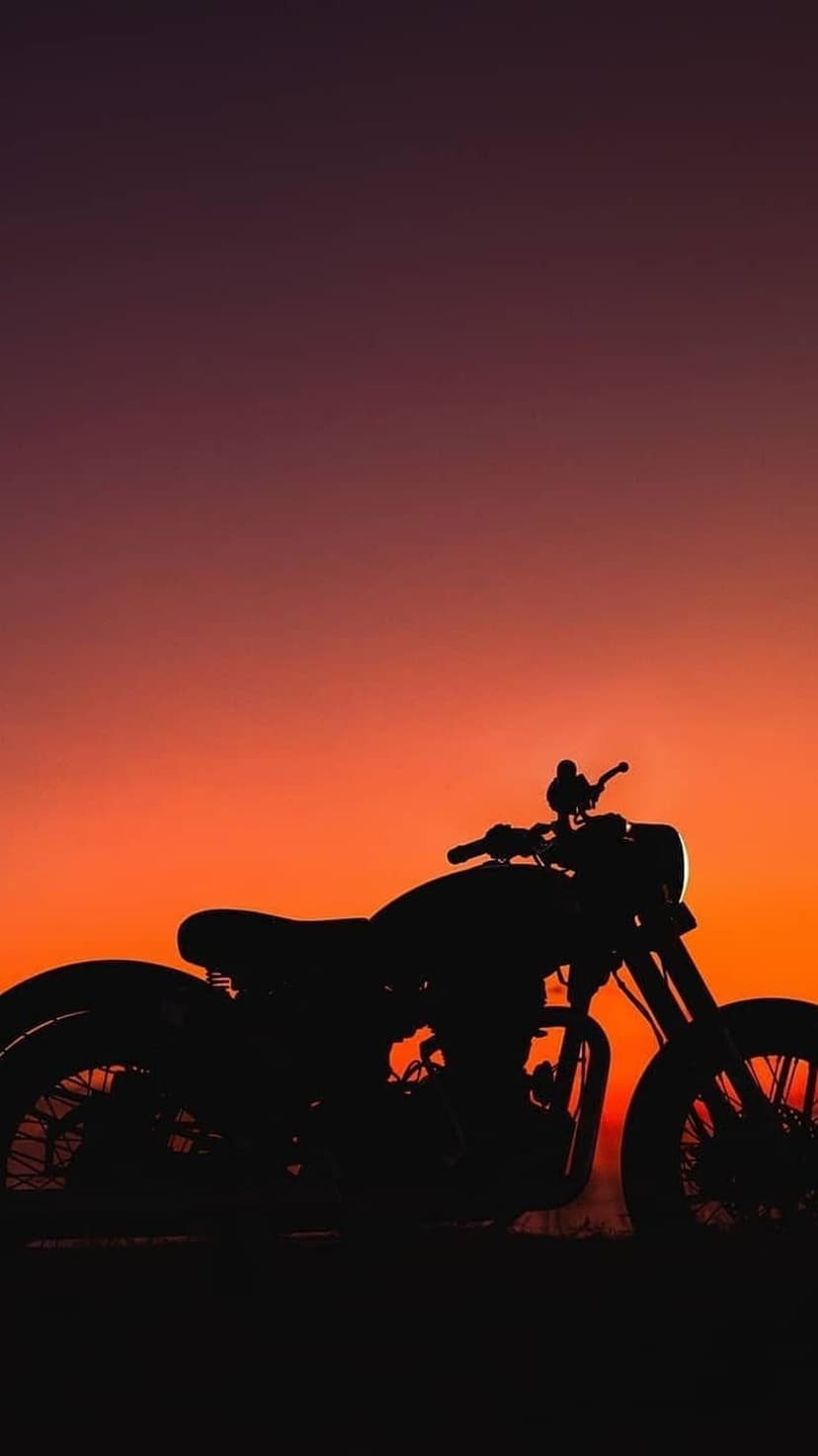 Vintage motorcycle silhouette with wire-spoke wheels against a purple and orange sunset sky at the horizon line.