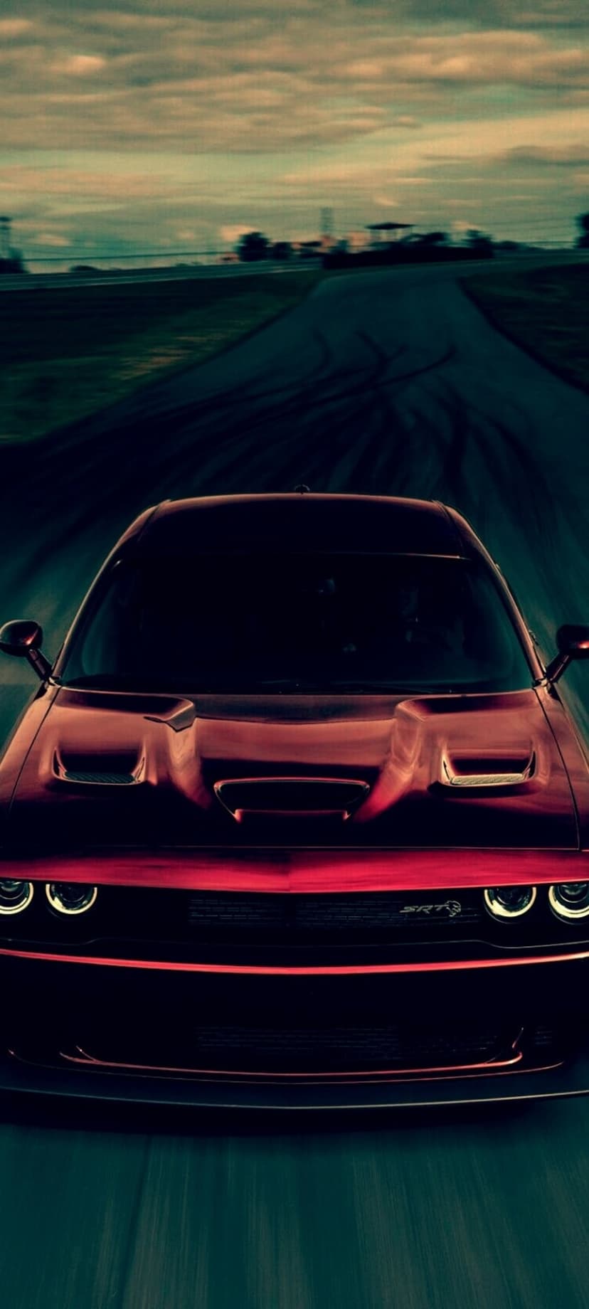 Red Dodge Challenger SRT with glowing headlights speeds on a dark road with streaks of motion blur at night.