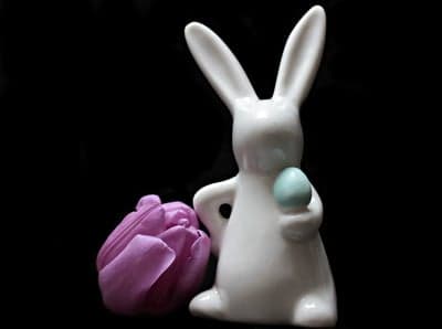 White Easter Bunny Figurine Holding Blue Egg Beside Purple Tulip
