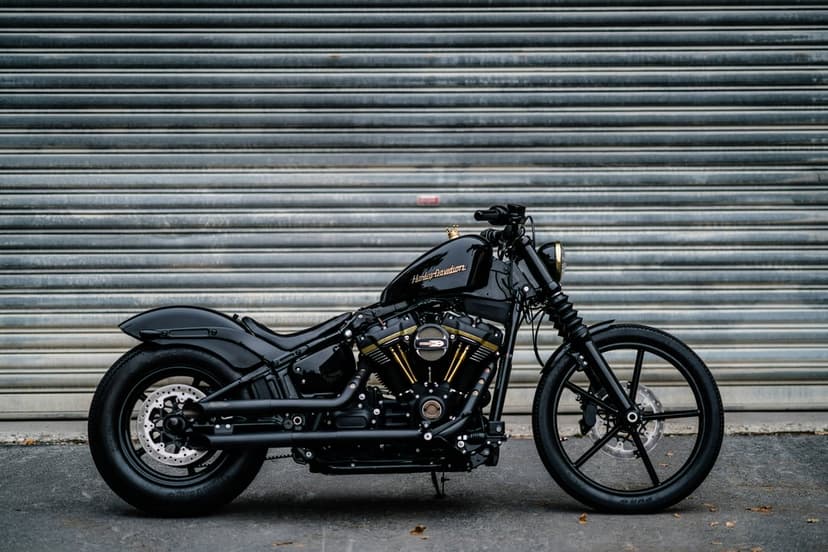 Black custom motorcycle with gold engine accents parked in front of a gray corrugated metal roll-up garage door.