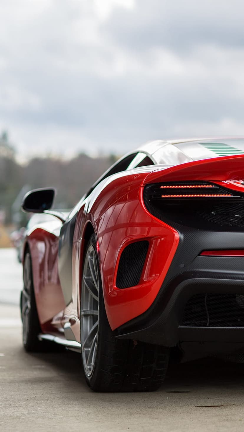 Red McLaren supercar rear showing glowing LED taillights and carbon fiber diffuser against a muted sky.
