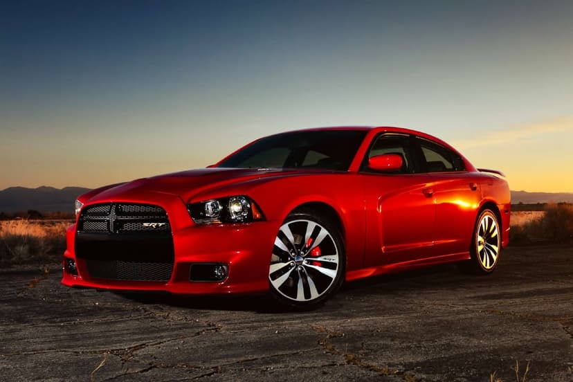 Red Dodge Charger SRT8 parked on cracked desert ground during a golden sunset with distant mountain peaks.
