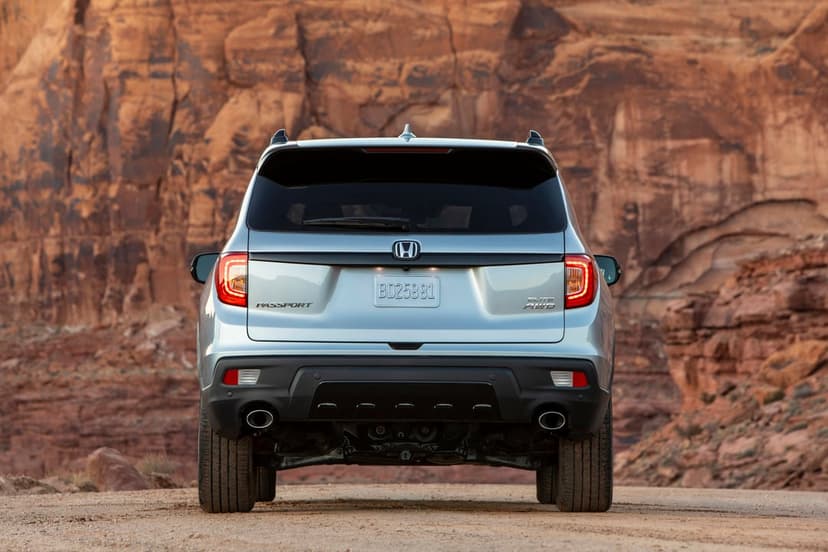 Rear view of a silver Honda Passport SUV on a desert road with massive red rock cliffs in the background.