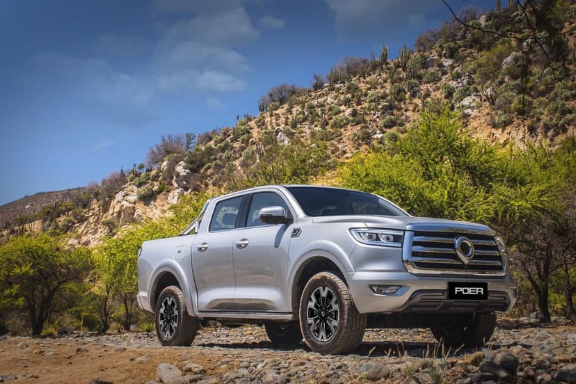 Silver GWM Poer pickup truck parked on a rocky dirt path with cactus-covered hills under a blue sky.