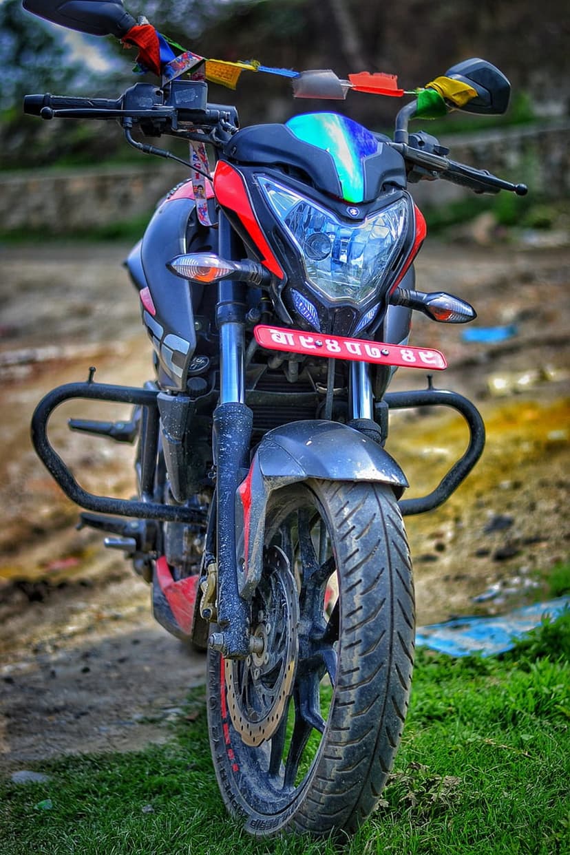 Red sport motorcycle with colorful prayer flags on handlebars and a black crash guard shot from a low angle.