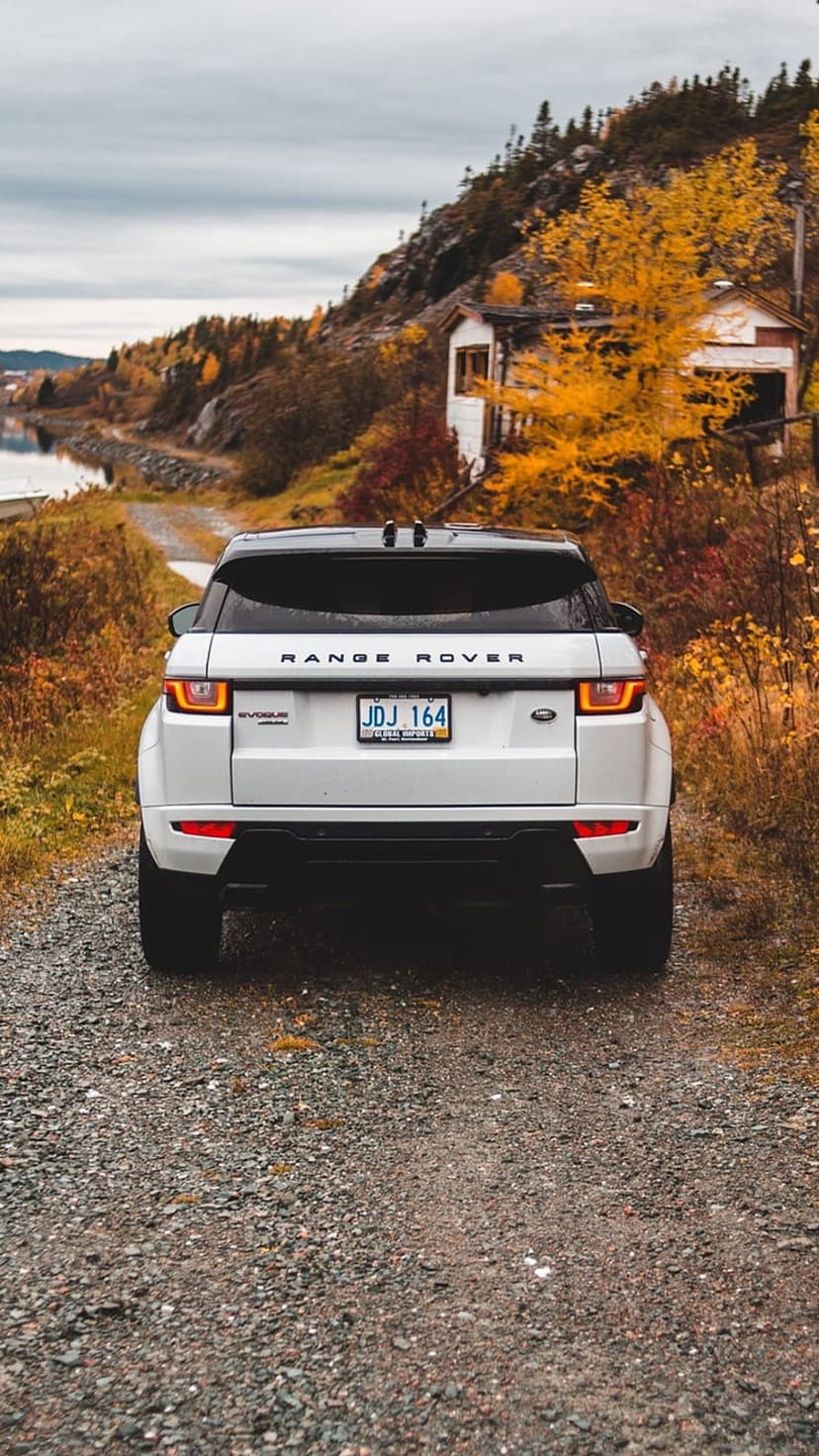 White Range Rover Evoque rear on a gravel road surrounded by orange autumn trees, a lake, and a small house.