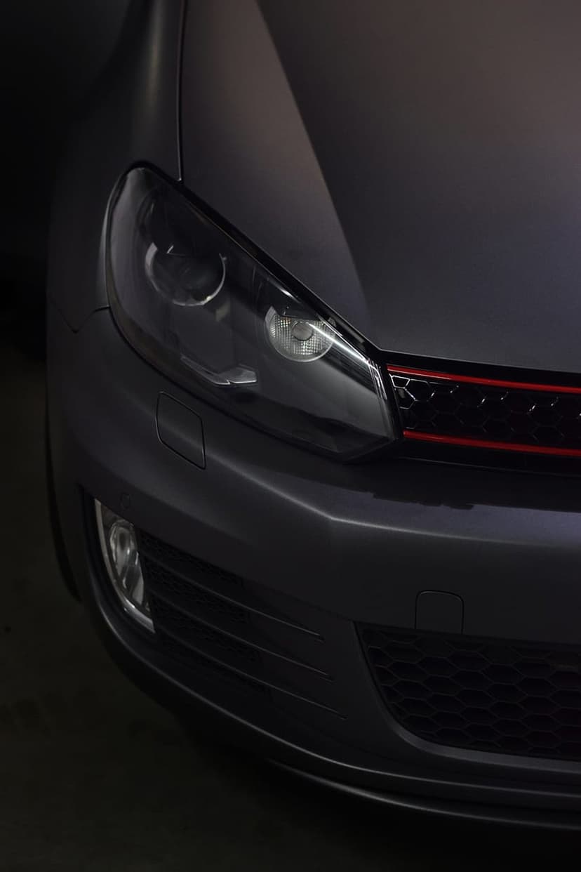 VW GTI front headlight and red accented honeycomb grille with a matte grey finish and dramatic low-angle lighting.