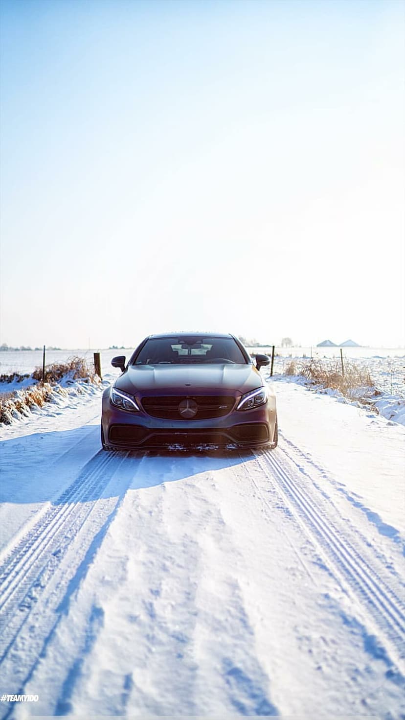 Dark Mercedes-Benz sedan parked on a snowy road with deep tire tracks under a clear blue sky in winter.