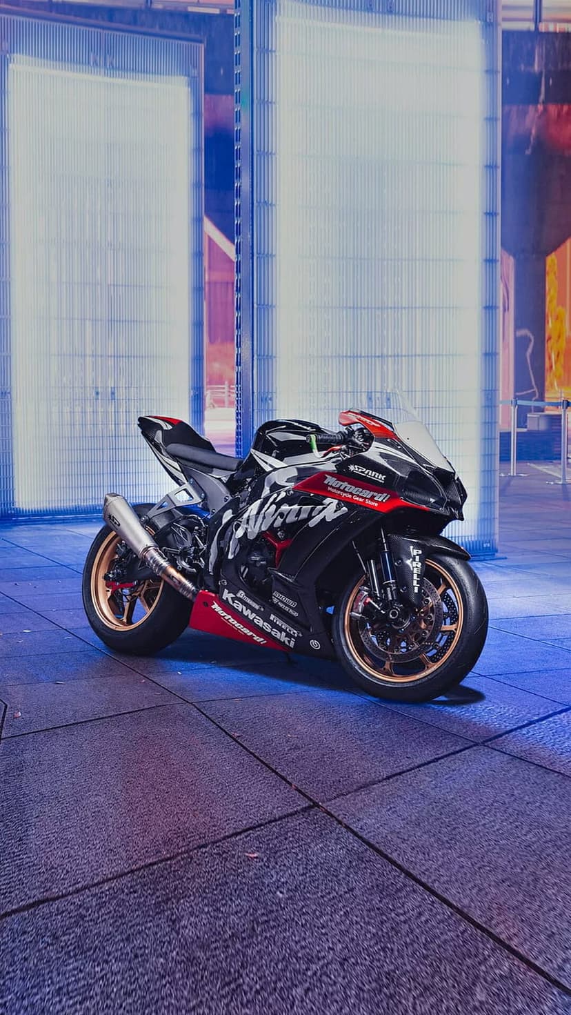 Black Kawasaki Ninja sportbike with red accents and gold rims rests on a glowing blue and purple tiled floor.