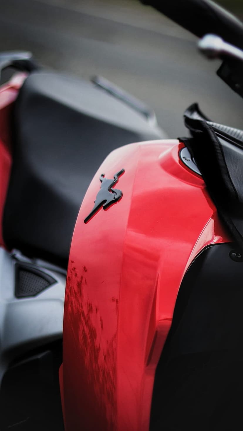 Red motorcycle fuel tank with a black figure emblem, glossy reflections, and a dark textured seat background.