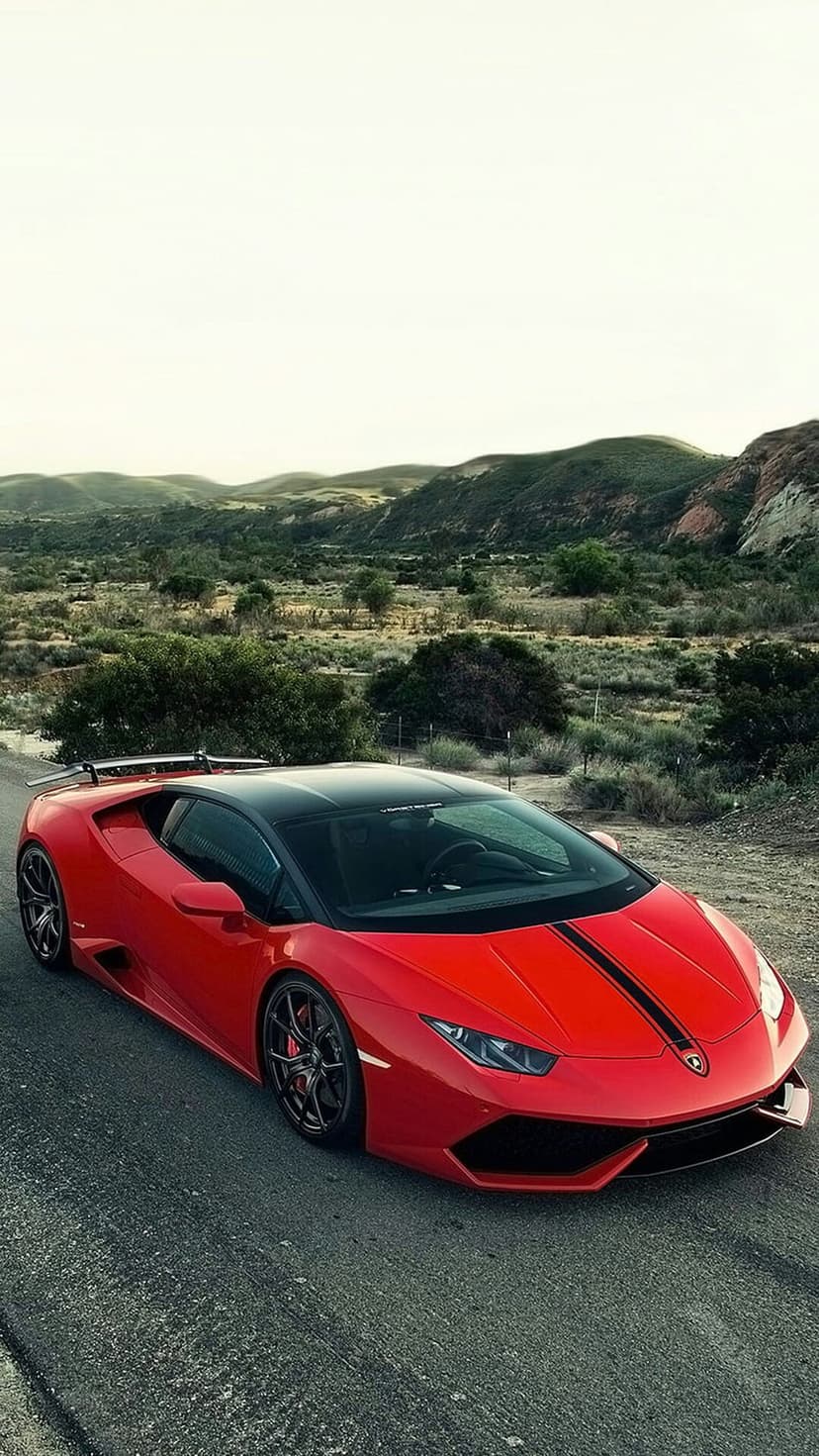 Red Lamborghini with black racing stripes parked on a dusty mountain road against a hazy, arid mountain backdrop.