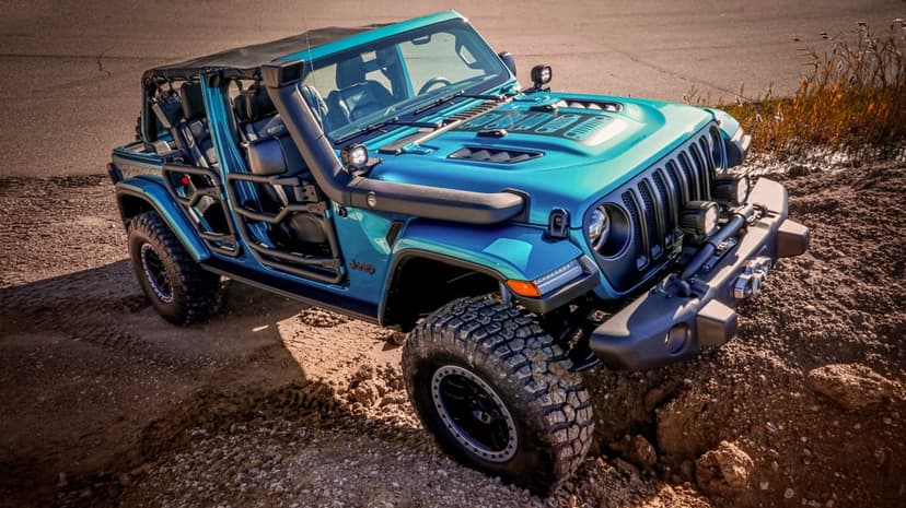 Teal Jeep Wrangler with tube doors and snorkel climbing a dirt mound during sunset with off-road lighting.