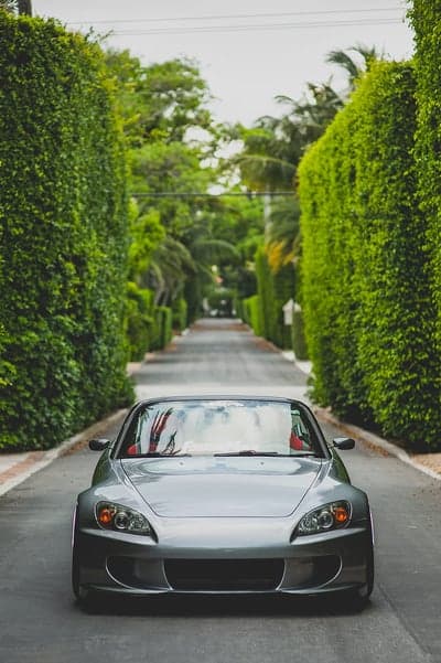 Silver Honda S2000 drives down lush green tree-lined driveway