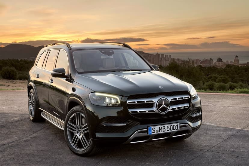 Black Mercedes-Benz GLS SUV parked on a ridge overlooking a coastal city during a warm golden hour sunset.