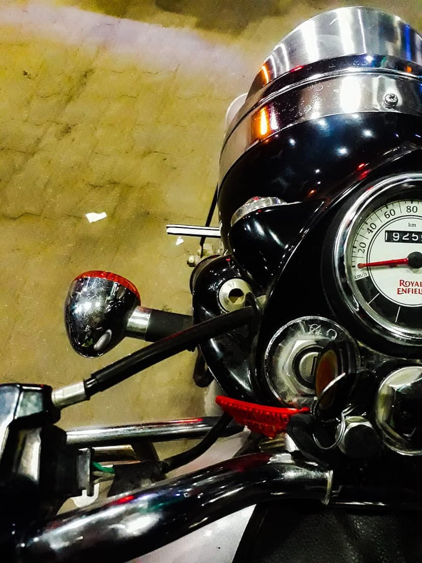 Royal Enfield chrome speedometer and handlebars against a textured wall with a red indicator light detail.
