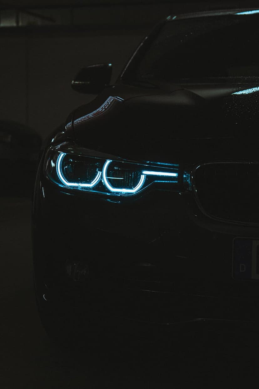 BMW front grille and glowing blue LED headlights emerge from a dark, shadowed background in a close-up shot.