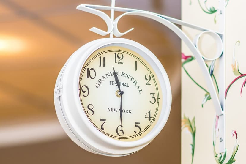 White Grand Central Terminal clock on an ornate bracket against light floral wallpaper in a portrait view.