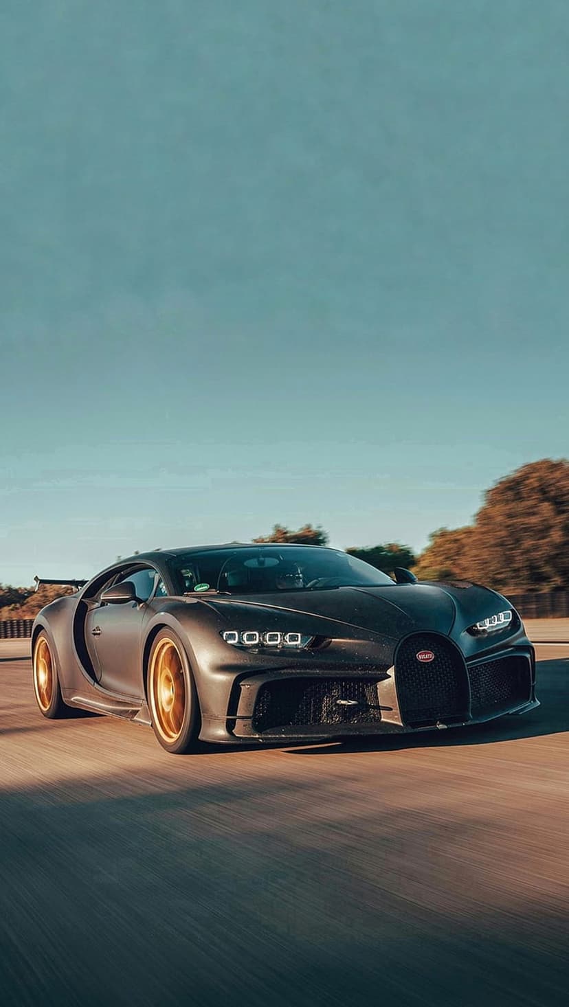 Bugatti Chiron Super Sport 300+ hypercar with gold wheels driving fast under a clear blue sky on a paved road.