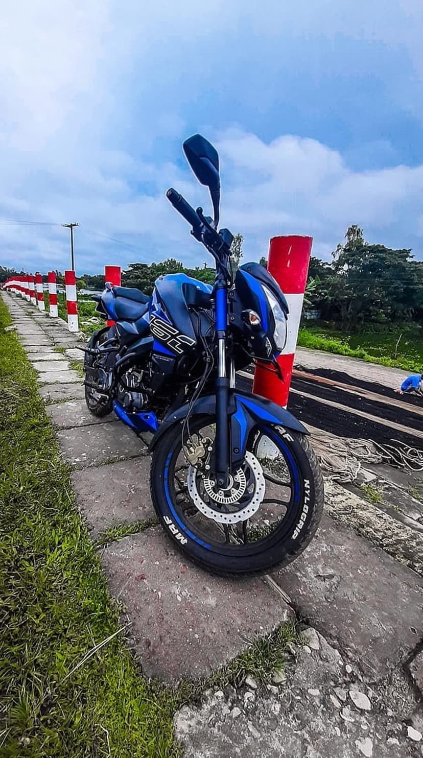 Blue and black sports bike on a stone path next to a red bollard under a cloudy sky in vertical orientation.
