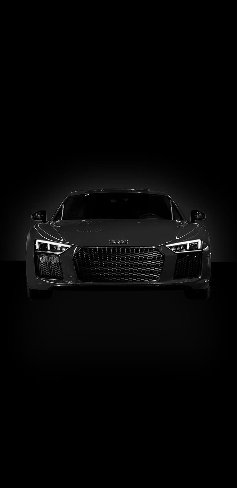 Audi R8 front grille and LED headlights emerge from a dark shadow in this black and white high-contrast photo.