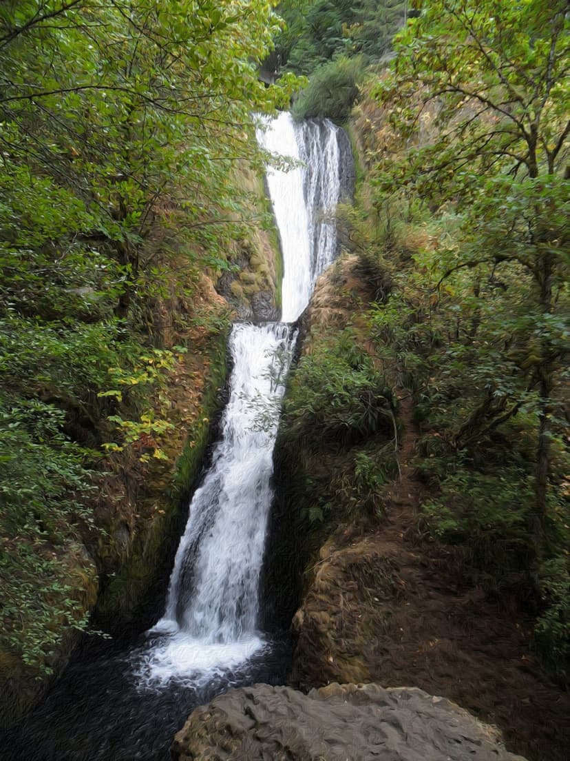 Multnomah Falls drops over basalt cliffs into a lush green canyon with a stone bridge between two tiers of water.