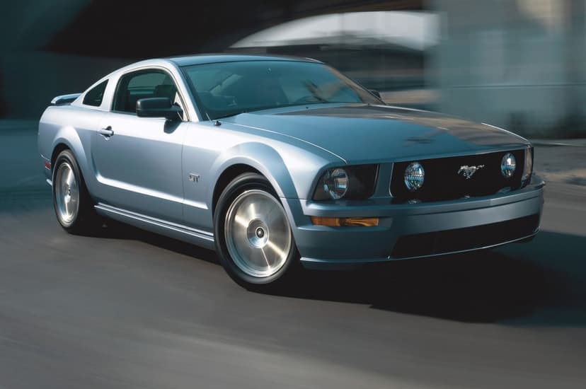 Silver Ford Mustang GT muscle car driving at high speed with motion blur on a city road in daylight.