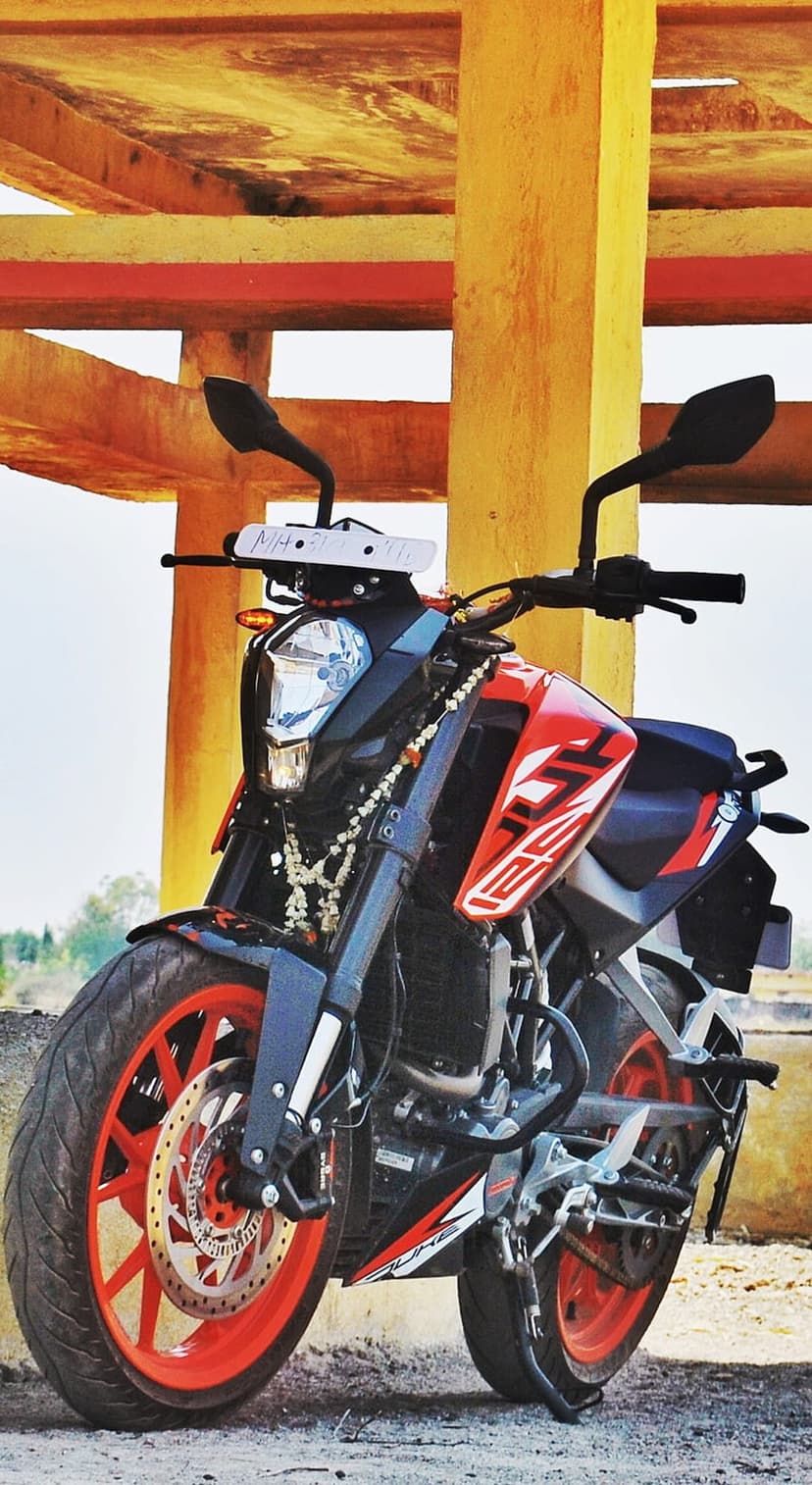 KTM 125 Duke motorcycle with orange rims parked under a yellow industrial structure on a concrete floor.